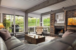 Ein modernes Wohnzimmer mit Kamin, Ledersofas, einem Couchtisch und großen Fenstern mit Blick auf einen Garten.