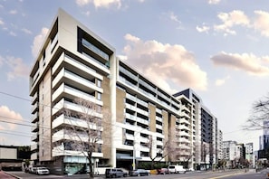 Monikerroksinen rakennus, jossa on parvekkeita, autotallin sisäänkäynti ja kirkas taivas.