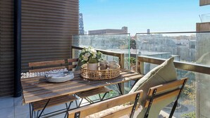 A balcony with a wooden table set for dining, a wicker basket, and a view of the cityscape.