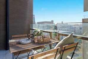 Ein Balkon mit Holztisch, gedecktem Esstisch, einem Korbwägelchen und Blick auf die Stadtlandschaft.