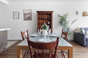 A dining area with a glass-top table, wooden chairs, a white vase with flowers, and a wooden cabinet in the background.