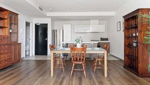 A modern kitchen with white cabinets, a dining table with chairs, and a wooden cabinet with plants.