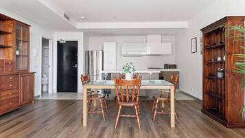 A modern kitchen with white cabinets, a dining table with chairs, and a wooden cabinet with plants.