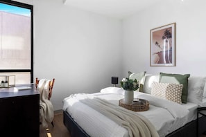 A bedroom with a bed, a desk, a chair, a window, and a framed picture on the wall.