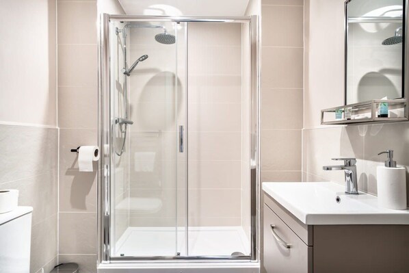 Une salle de bain moderne avec une douche à parois de verre, un lavabo blanc et un miroir au-dessus du lavabo.