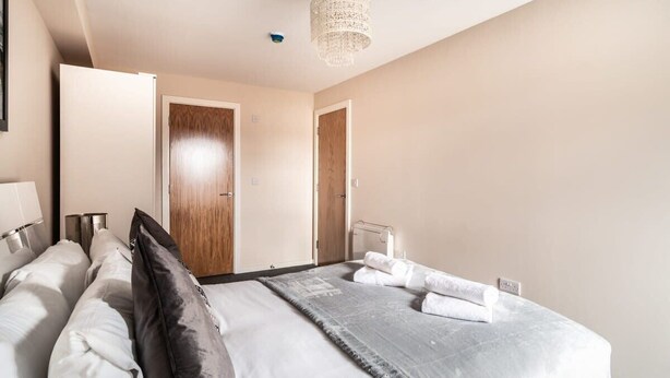 A modern hotel room with a large bed, a wooden door, and a chandelier. - Spacious & Bright 2 Bed Apartment in Manchester (Manchester)
