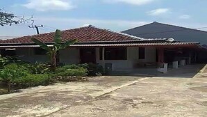 Una casa de dos pisos con techo de tejas, entrada de concreto y un pequeño jardín con plantas.