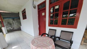 Una habitación con suelo de baldosas, una mesa con mantel estampado, dos sillas y una puerta roja.