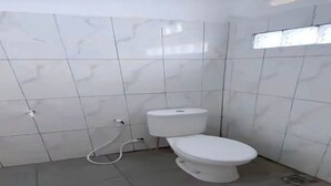 Un baño pequeño con azulejos, un inodoro blanco y un enchufe a la vista.