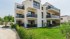 A modern multi-story residential building with balconies, a well-maintained lawn, and a clear sky. - Modern Studio Apartment Valla I with Terrace and Garden view (Funtana)