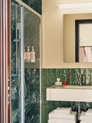 A bathroom with a glass-enclosed shower, a sink with a mirror above it, and green tiled walls. - Numa Rome Barberini (Rome)