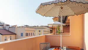 A balcony with a striped umbrella, a table with a book and glasses, and a chair. - Numa Rome Barberini (Rome)