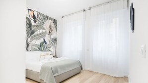 Un dormitorio con cama, un cuadro grande y cortinas translúcidas.