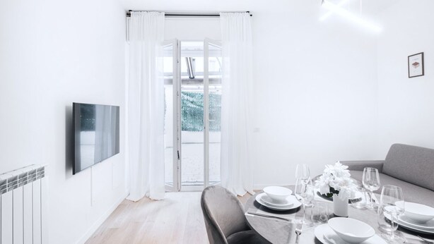 Un comedor moderno con una mesa dispuesta para dos personas, un sofá y un televisor montado en la pared.