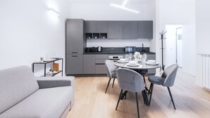 Una cocina moderna con armarios grises, una mesa de comedor preparada para dos personas y un sofá gris en la sala de estar.