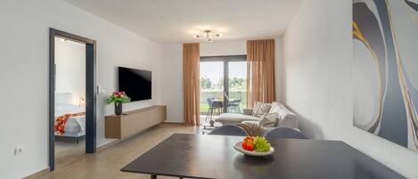 Een moderne woonkamer met een flatscreen televisie, een eettafel met stoelen, een bank en een balkon met zitplaatsen buiten.