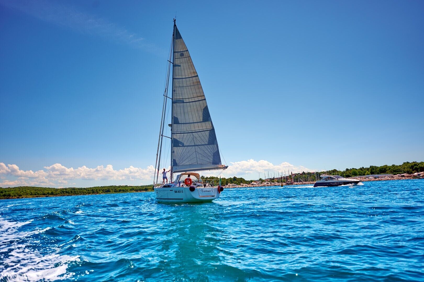 Un velero en un mar azul despejado con una costa lejana.
