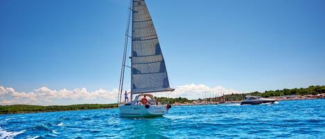 Un velero en un mar azul despejado con una costa lejana.