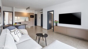 Una sala de estar moderna con un televisor de pantalla plana grande, un sofá y un comedor con una cocina al fondo.