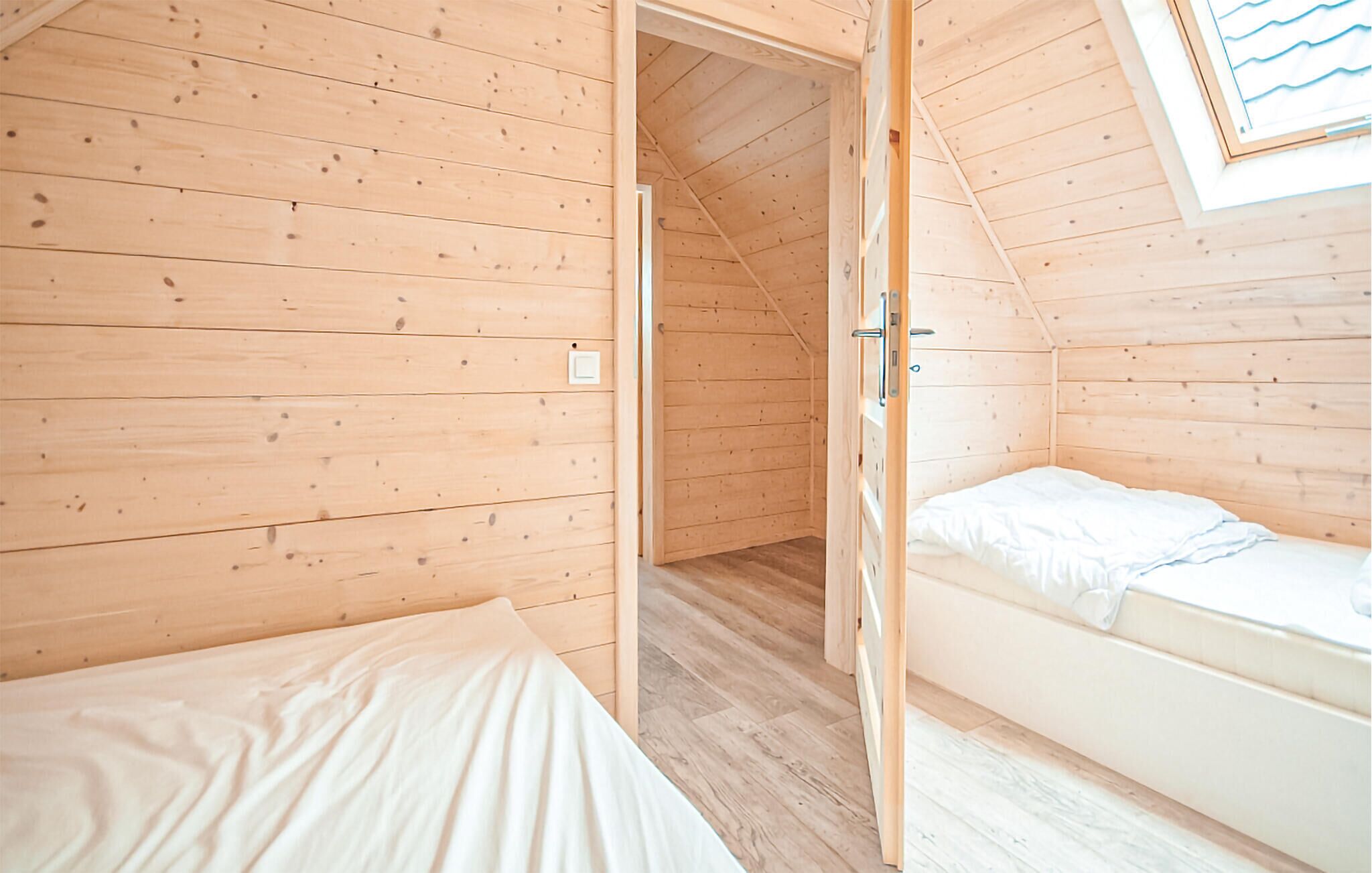 A small, wooden cabin with two beds, a wooden floor, and a sloped ceiling.