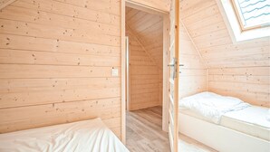 Een klein, houten huisje met twee bedden, een houten vloer en een schuin dak.