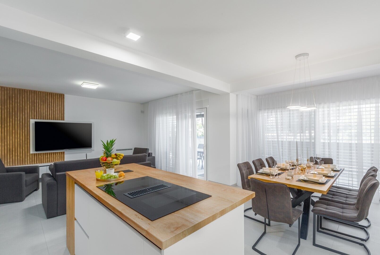 Ein modernes Wohnzimmer mit einem Holzespeisetisch, grauen Sofas und einem Flachbildfernseher, der an einer Wand aus Holzpaneelen befestigt ist.
