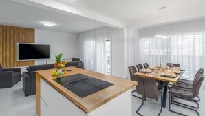 Un salon moderne avec une table à manger en bois, des canapés gris et un téléviseur à écran plat fixé sur un mur recouvert de panneaux en bois.