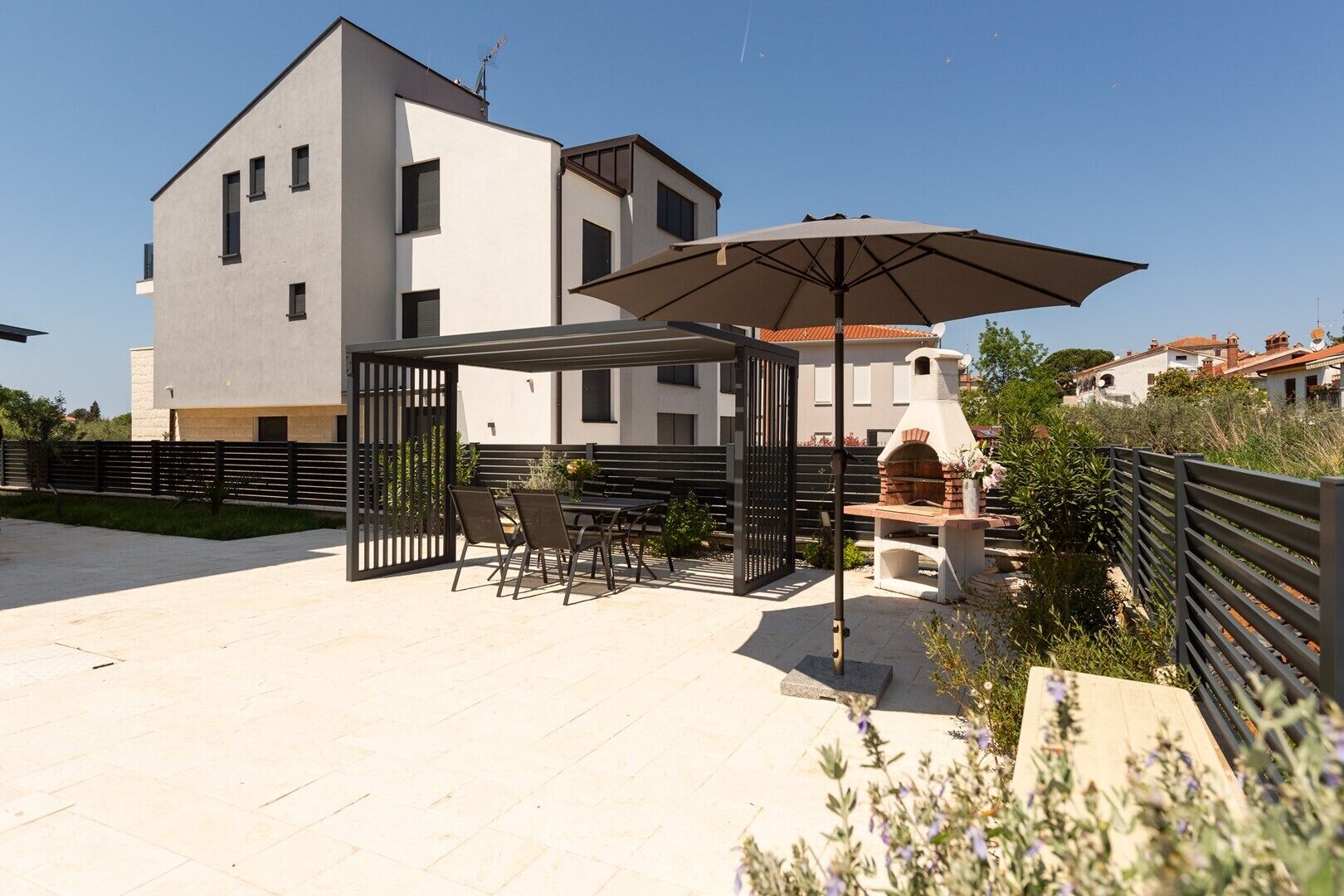 A modern outdoor patio with a pergola, seating, and a brick oven.
