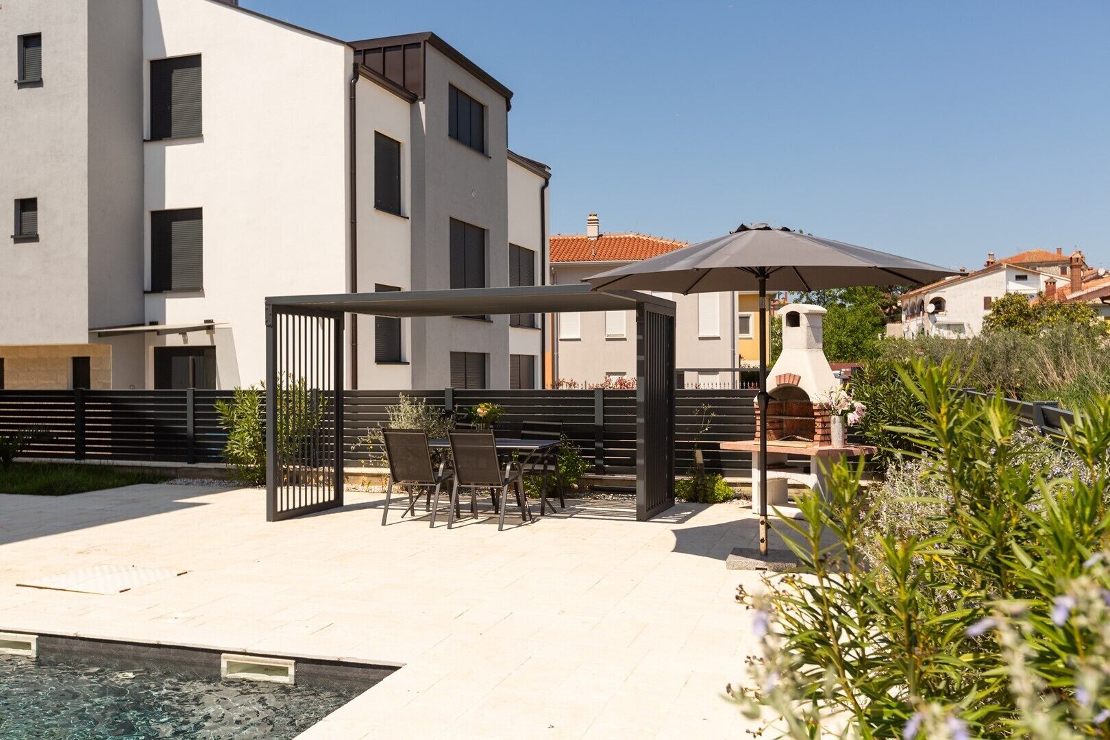 A modern outdoor patio with a table and chairs, a grill, and a pool area.