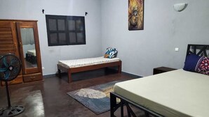 Un dormitorio con cama, un banco, un ventilador, una ventana y un cuadro en la pared.
