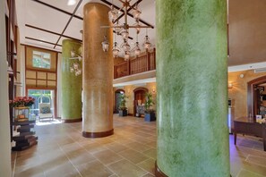 Um hall amplo com grandes colunas verdes, uma escadaria e um candelabro.