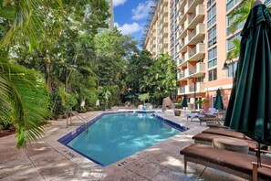 Piscina rodeada por espreguiçadeiras e guarda-sóis, com um edifício ao fundo.
