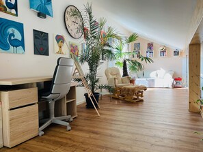 Relax in this stylish room with a large desk, comfortable armchair, and small bed, surrounded by artwork and lush greenery.