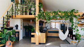A spacious loft with a mezzanine level, wooden staircase, and abundant indoor plants.