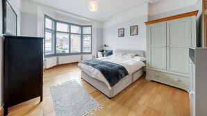 Ein Schlafzimmer mit einem Bett, einem Schreibtisch, einem Kleiderschrank und großen Fenstern.