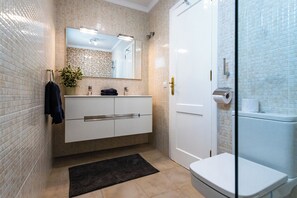 A modern bathroom with a white vanity, a large mirror, a glass shower enclosure, and a beige tiled wall. - Luxury Villa with Stunning Ocean & Mountain View’s (Montaña Roja)