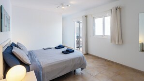 A bedroom with a bed, a bedside table, a lamp, a window with curtains, and a view of the outdoors. - Luxury Villa with Stunning Ocean & Mountain View’s (Montaña Roja)
