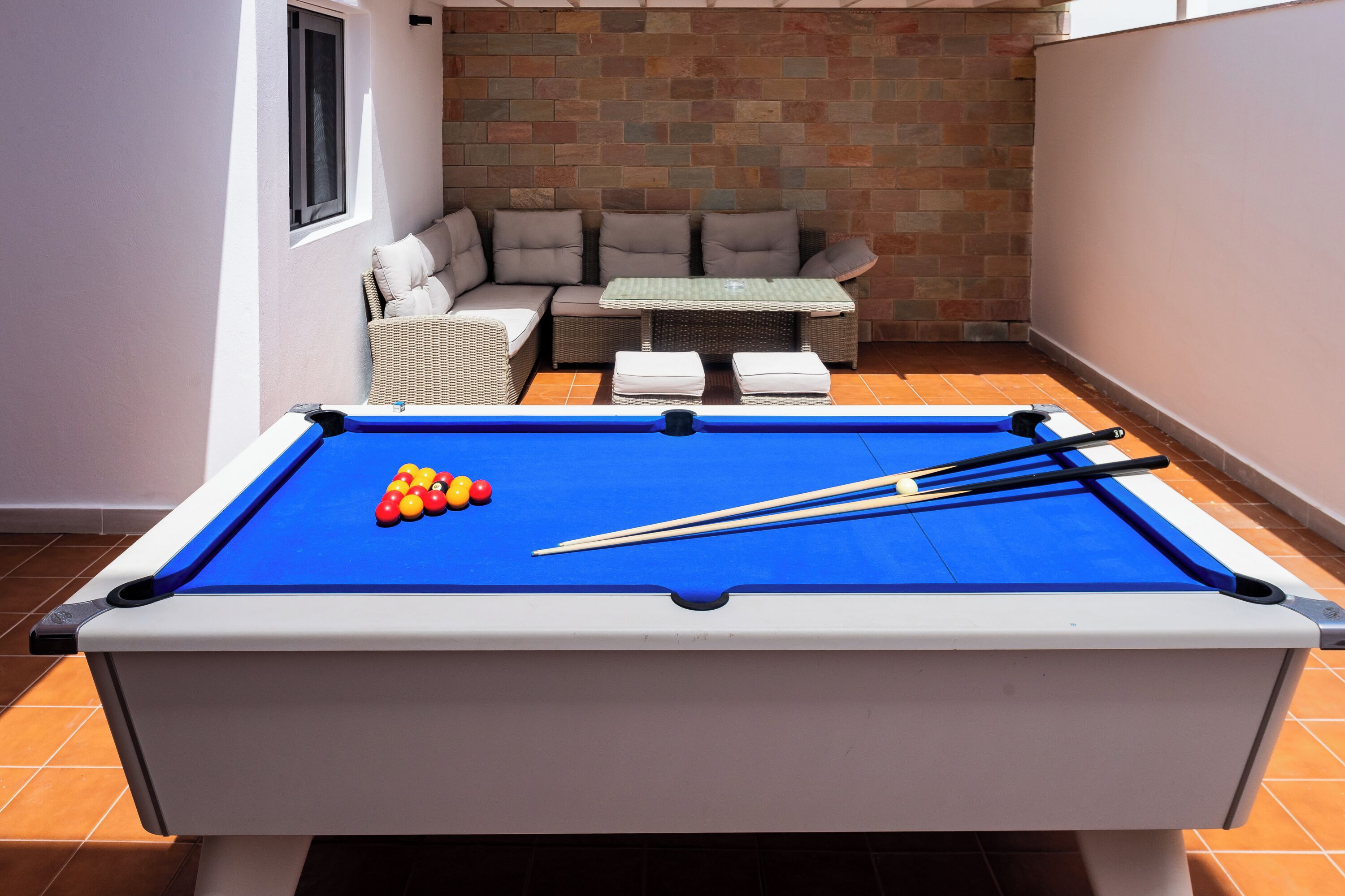 A pool table with balls and cues, a sofa, and a brick wall.