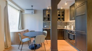 Une cuisine moderne avec des meubles de couleur sombre, un plan de travail en marbre et un four encastré. On y trouve également un coin repas avec une table ronde et quatre chaises.