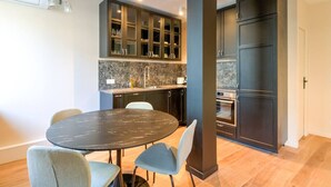 Une cuisine moderne avec des meubles de couleur sombre, un plan de travail en marbre et une table de salle à manger ronde, assortie de chaises.
