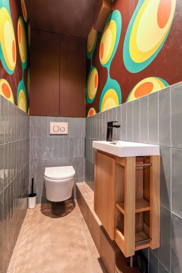 Un baño con inodoro, lavamanos y un armario. Las paredes tienen un motivo circular de colores.