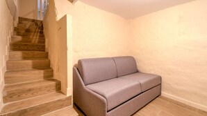 Une pièce avec un escalier en bois, un canapé gris et des murs de couleur neutre.