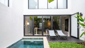 Une maison moderne dotée d’une piscine, d’un patio avec deux chaises longues et d’une porte vitrée donnant sur l’intérieur.