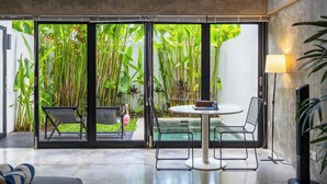 Un intérieur moderne avec une porte vitrée donnant sur un jardin luxuriant, une table ronde entourée de chaises et un téléviseur fixé au mur.