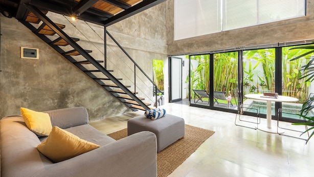 Un salon moderne avec un canapé gris, un escalier en bois et une grande fenêtre donnant sur un paysage verdoyant.