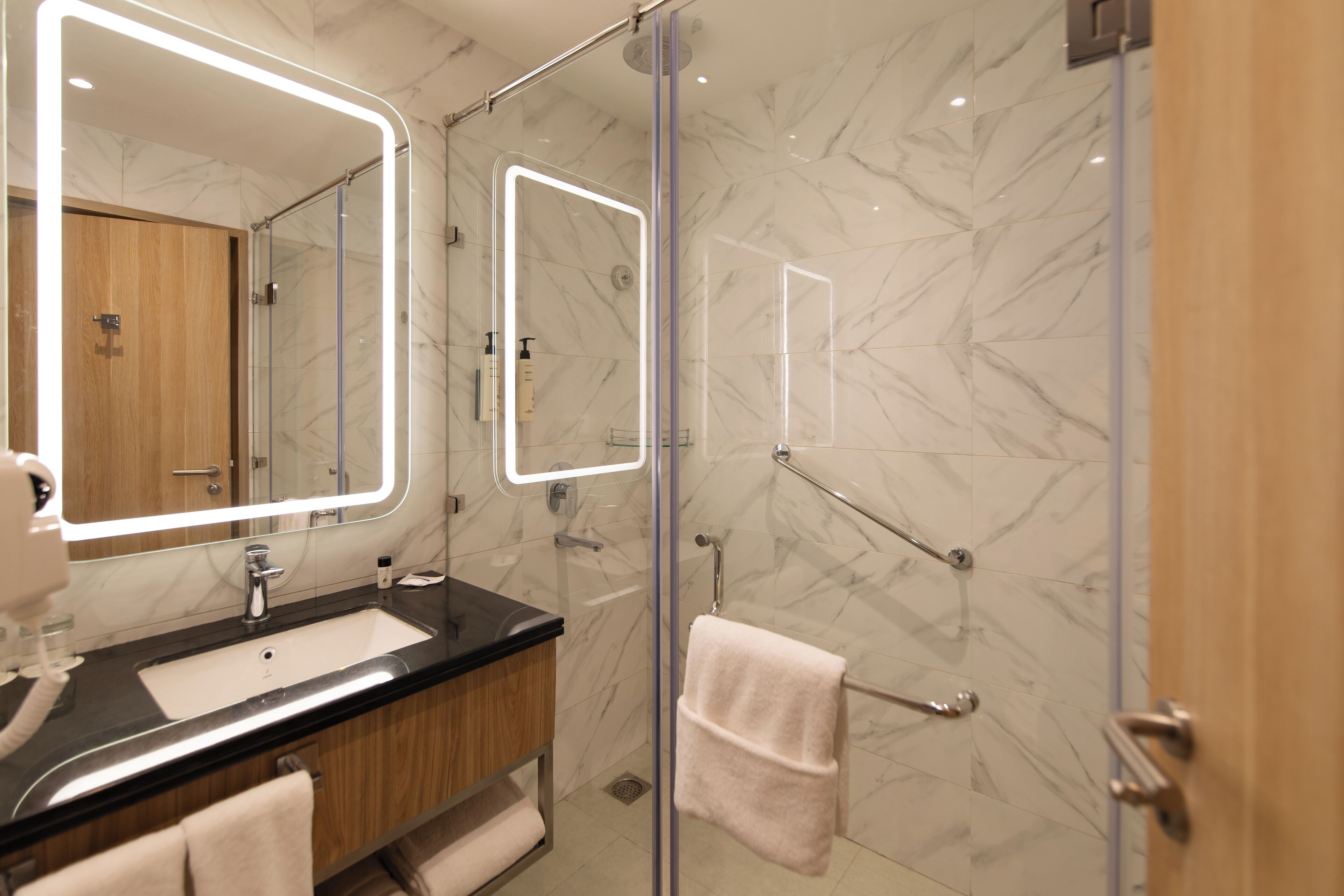 A modern bathroom with a glass-enclosed shower, a vanity with a sink, and a large mirror with integrated lighting.