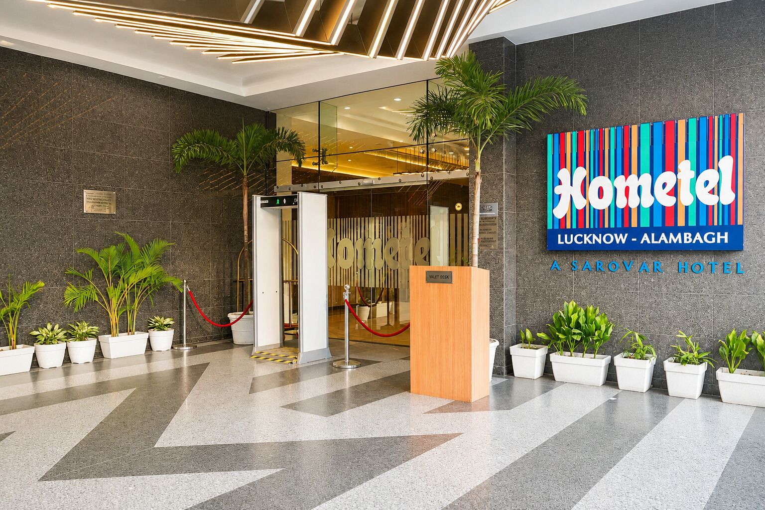 A hotel lobby with a modern design, a reception desk, and a sign for 'Hometel Lucknow - Alambagh Sarovar Hotel'.