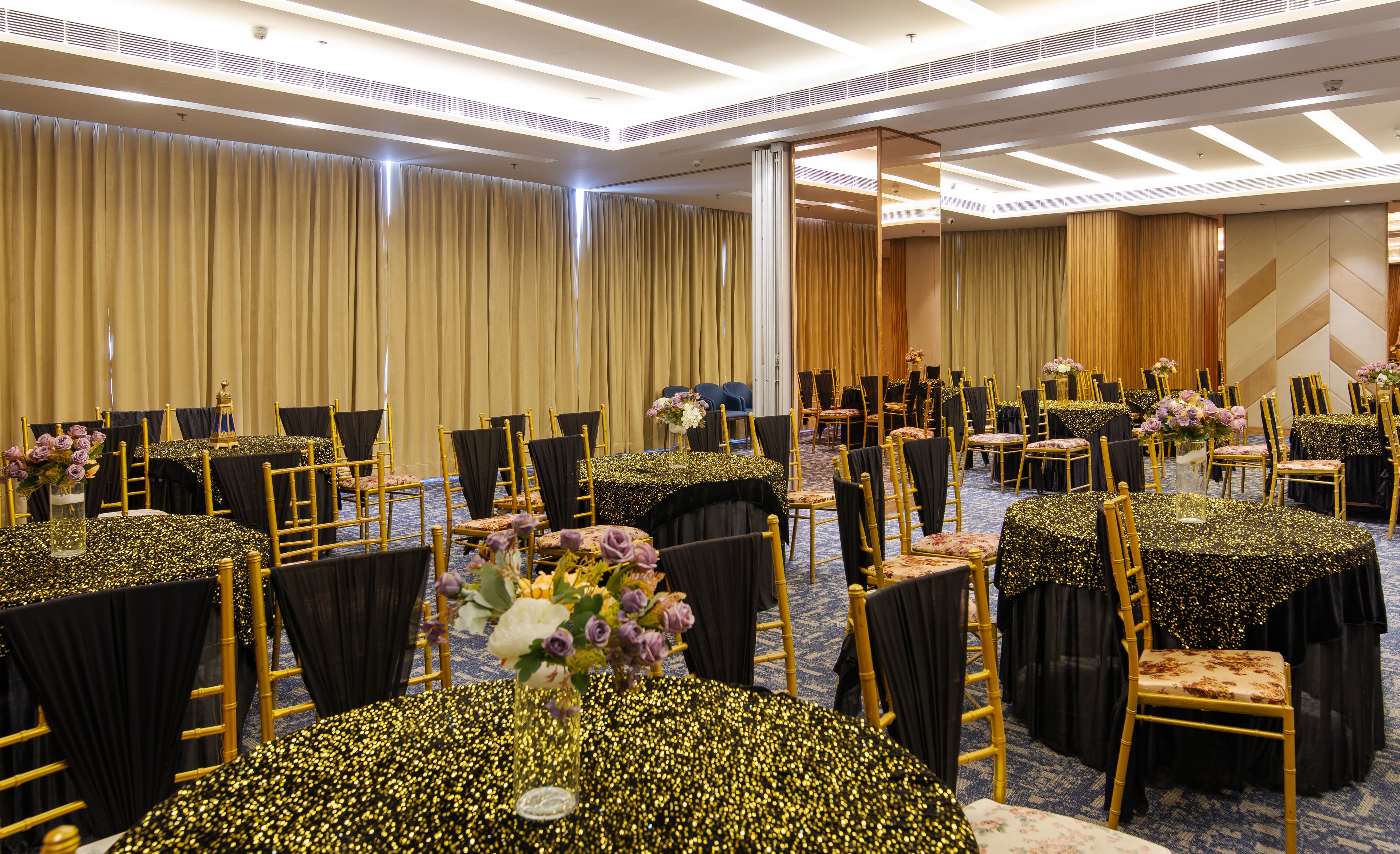 A conference room with rows of tables and chairs, each with a black tablecloth and gold chair.