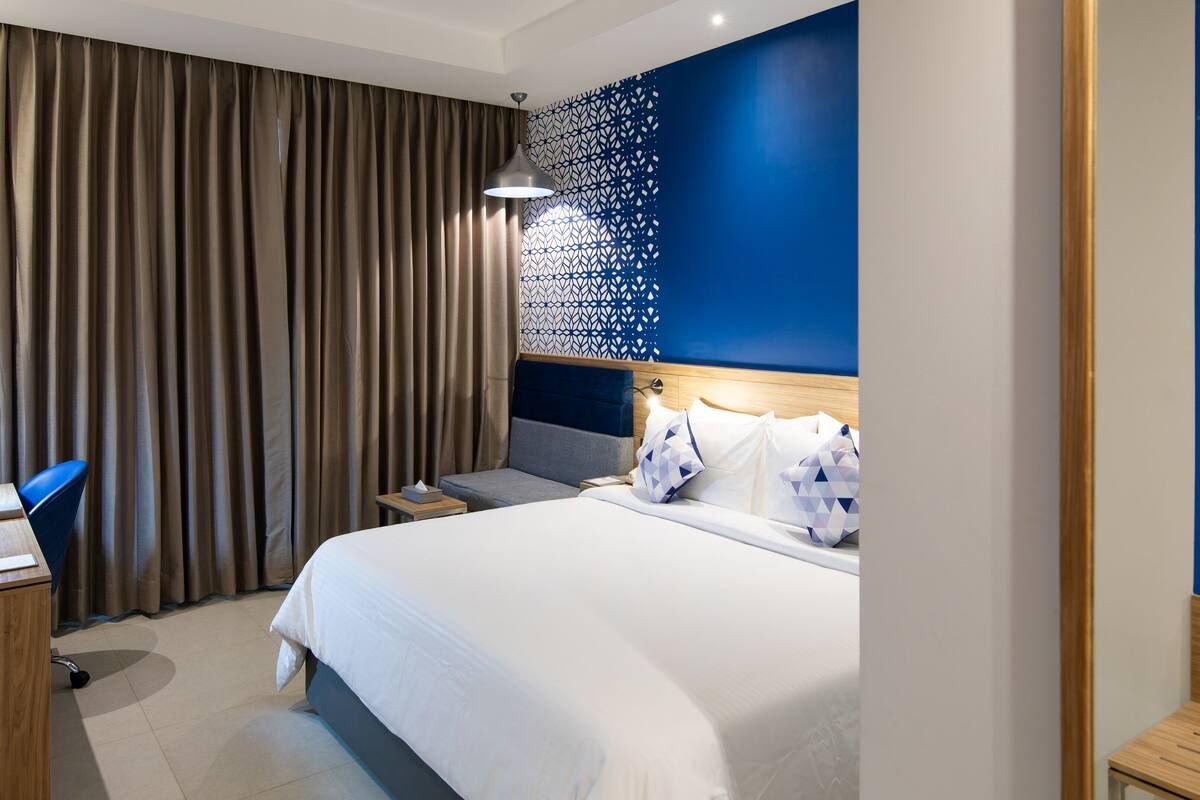 A modern hotel room with a large bed, a desk, and a chair.