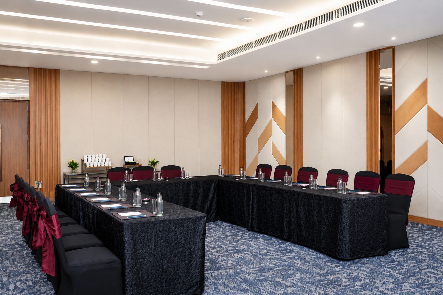 Un salón de conferencias con una larga mesa, sillas y una alfombra estampada.